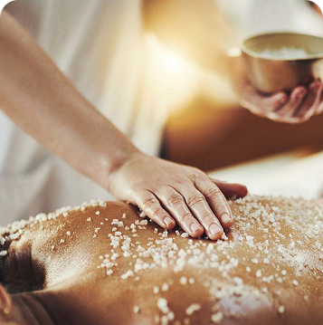 Terapis menaburkan scrub lulur ke punggung klien